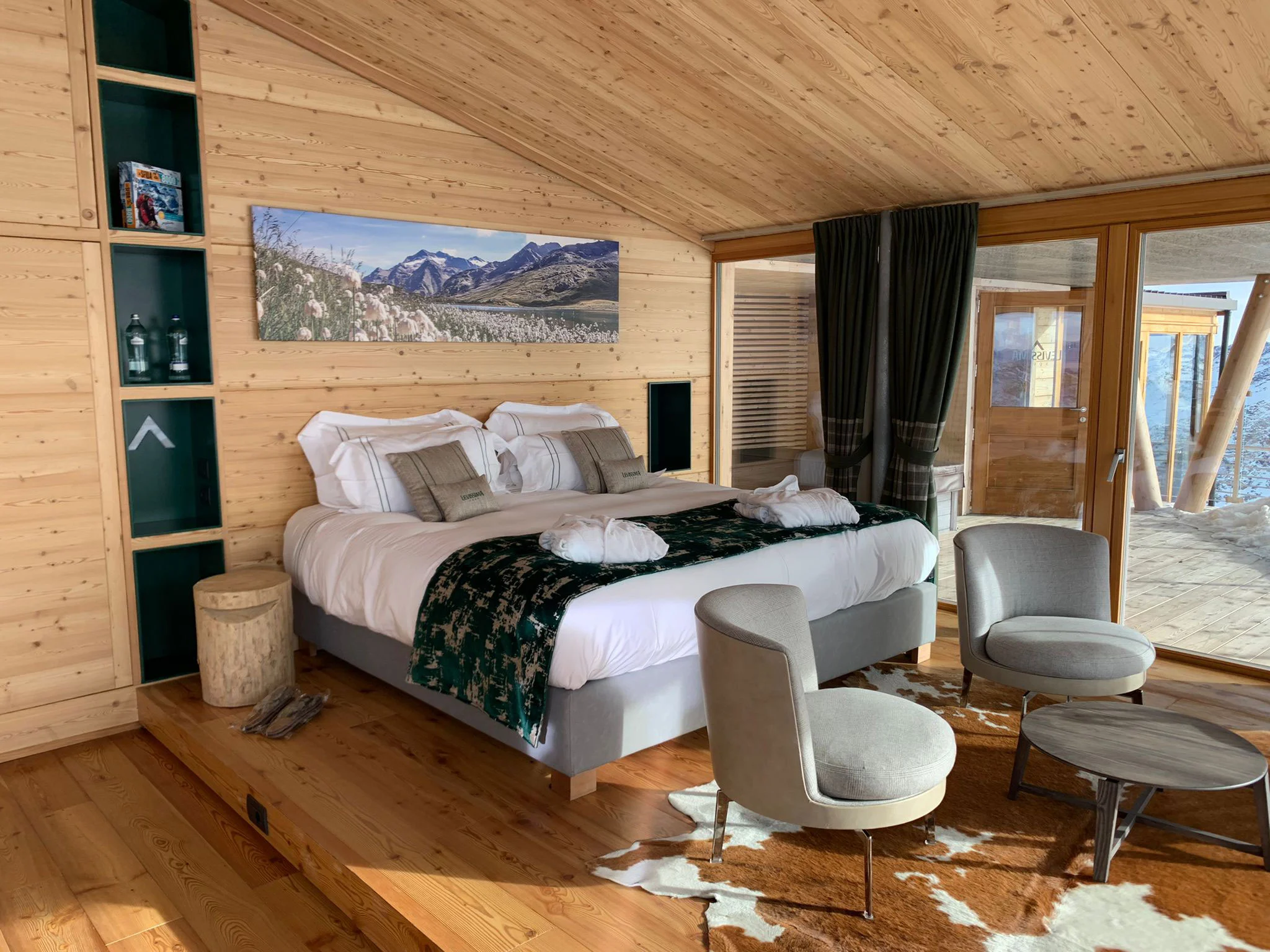 Camera rivestita in legno con letto matrimoniale su una pedana, una fotografia di montagna sopra e due poltrone – Levissima 3000 Chalet, Valdisotto, Italia, 2018 – architettura