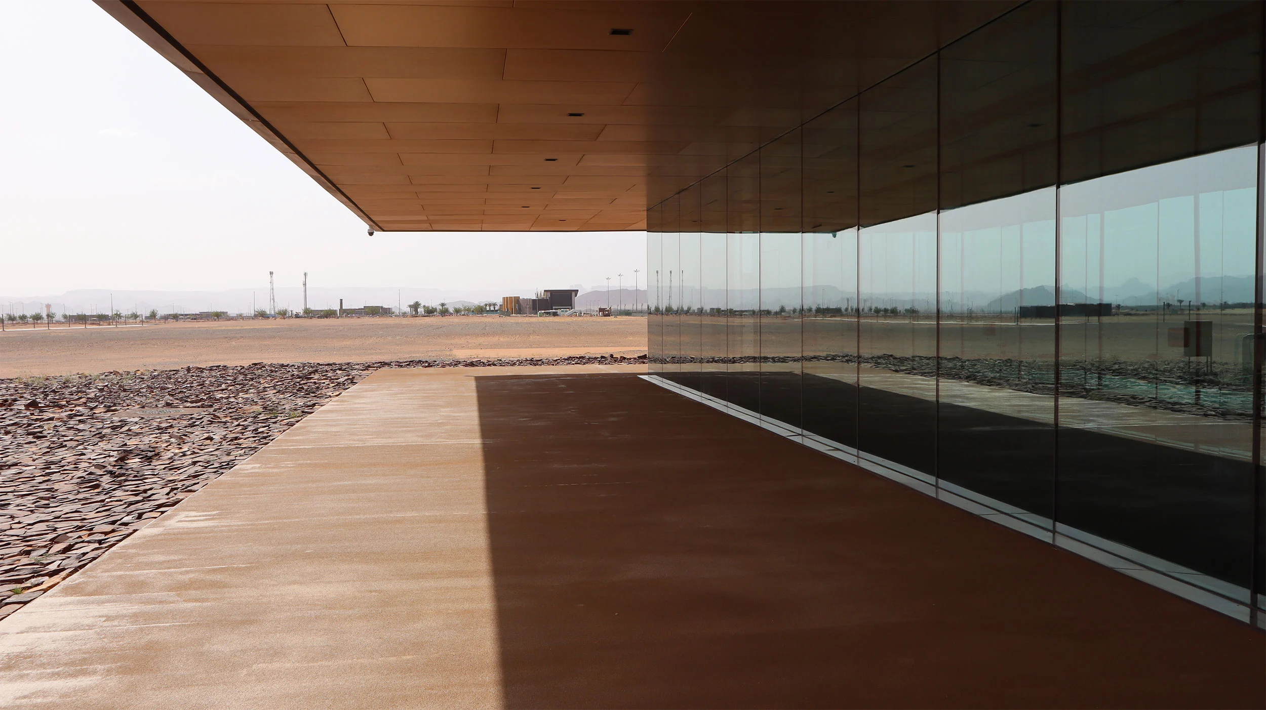 Percorso ombreggiato sotto la copertura a sbalzo, la facciata in vetro a specchio che riflette il deserto – Aeroporto Principe Abdul Majeed bin Abdulaziz, AlUla, Arabia Saudita, 2021 – architettura