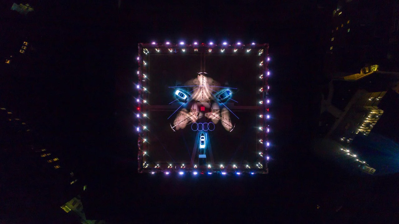 Vista aerea notturna del cortile dell'Audi City Lab: contorno quadrato luminoso, grafiche luminose a terra e auto – Audi City Lab al Fuorisalone, Milano, Italia, 2017 – progettazione di eventi