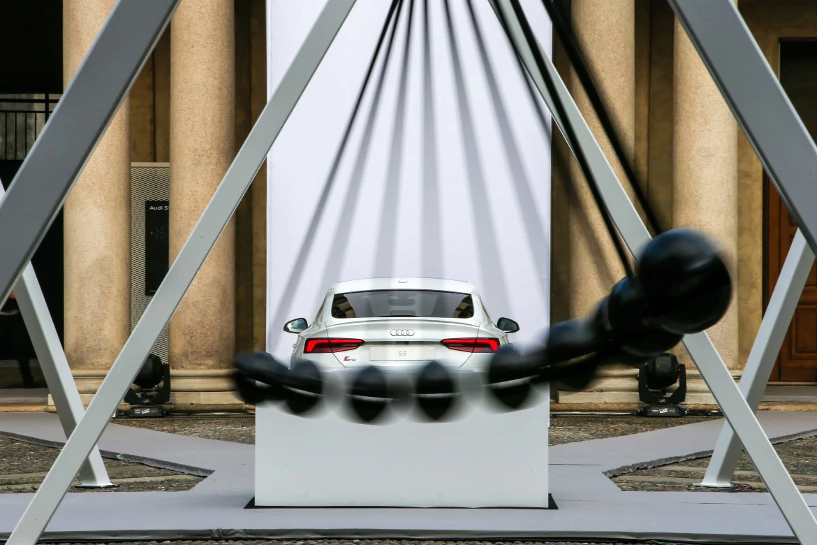 Audi bianca su un basamento vista attraverso un telaio d'acciaio, con un pendolo nero in movimento – Audi City Lab al Fuorisalone, Milano, Italia, 2017 – progettazione di eventi