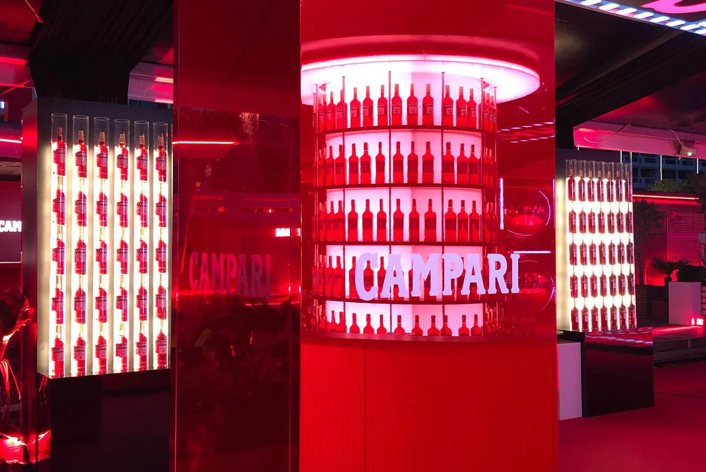 Mensole retroilluminate di bottiglie Campari su un espositore cilindrico e colonne a parete in luce rossa – Campari al 75° Festival di Cannes, Francia, 2022 – progettazione di eventi