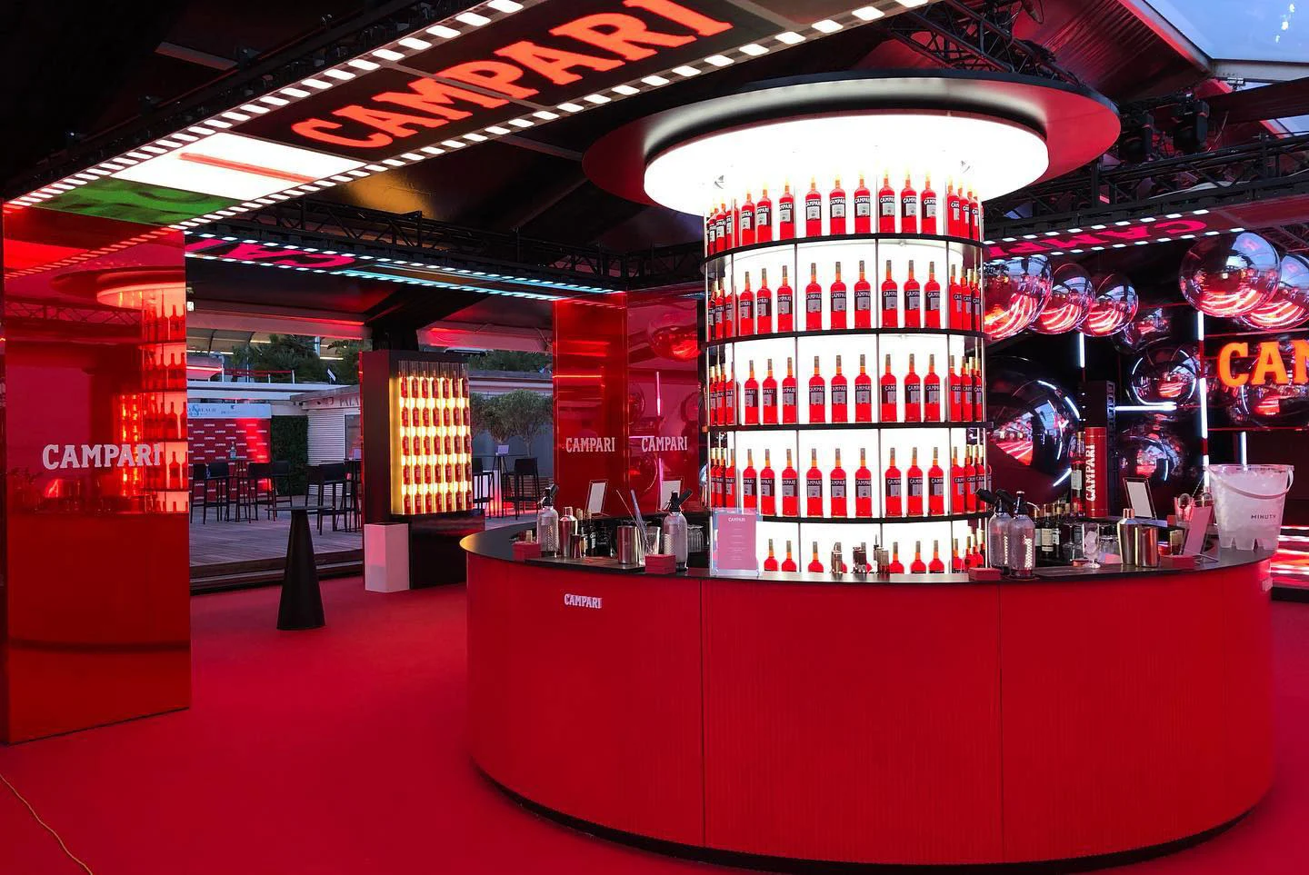 Bar circolare rosso Campari con una torre di bottiglie retroilluminata, circondato da sfere a specchio e colonne rosse – Campari al 75° Festival di Cannes, Francia, 2022 – progettazione di eventi