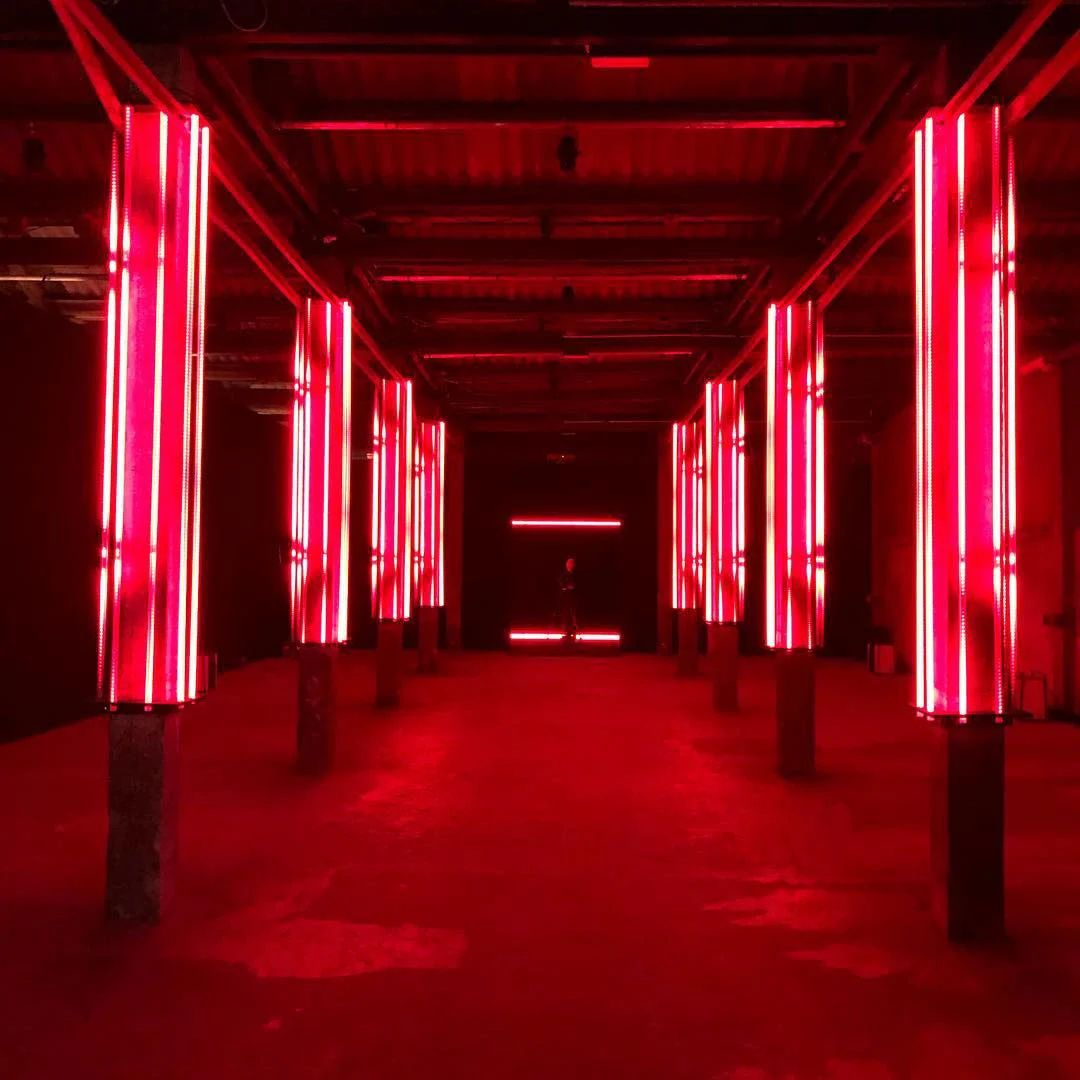 Lunga sala industriale in luce rossa, con pilastri avvolti da tubi al neon verticali – Campari Red Diaries, Milano, Italia, 2017 – progettazione di eventi