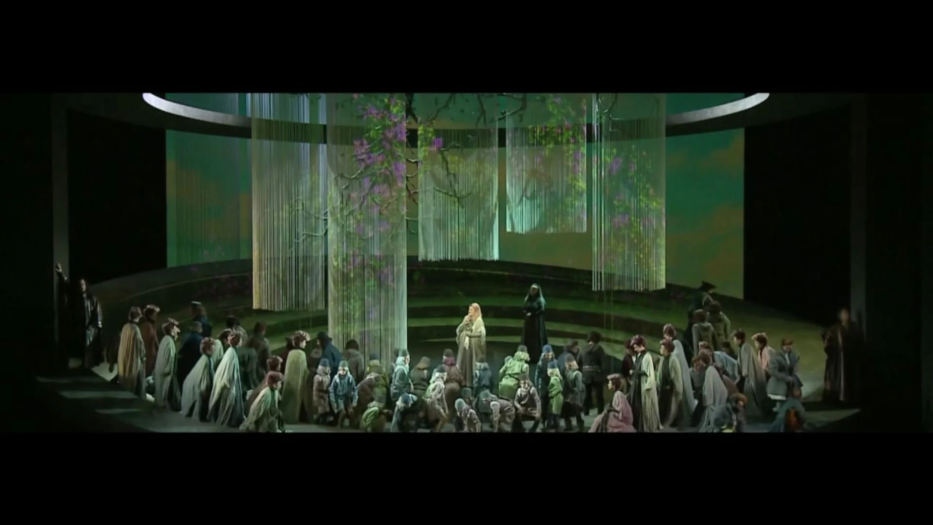 Coro riunito sul palco rotondo tra tende a fili su cui è proiettato un albero in fiore – Otello al Teatro Carlo Felice, Genova, Italia, 2014 – scenografia d'opera