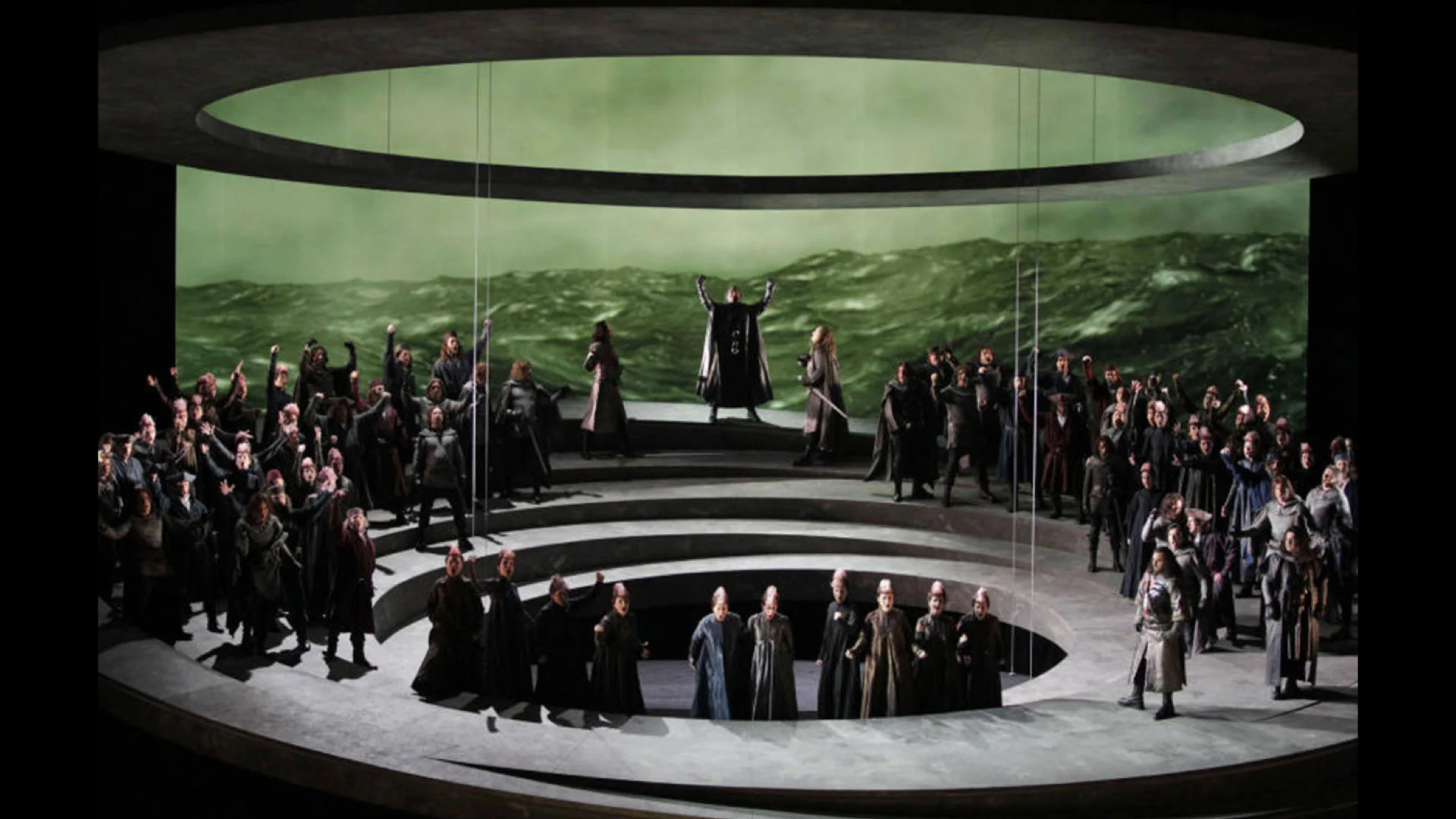 Otello al Teatro Carlo Felice: coro su gradoni circolari davanti alla proiezione di un mare in tempesta – Otello al Teatro Carlo Felice, Genova, Italia, 2014 – scenografia d'opera