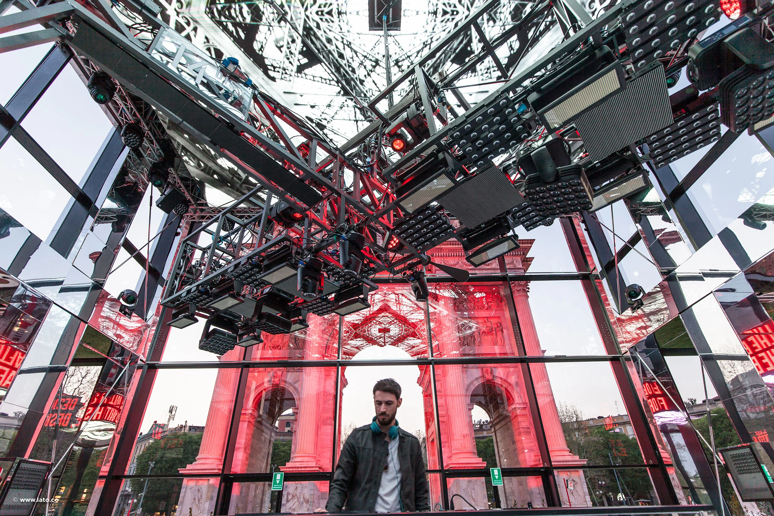 DJ sotto un'americana d'acciaio rossa con pannelli luminosi, l'arco visibile attraverso le pareti di vetro – Cartier The Legendary Thrill, Milano, Italia, 2018 – progettazione di eventi