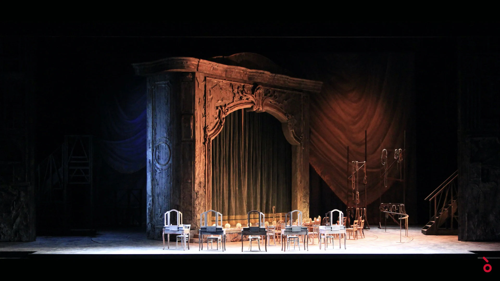 Portale intagliato con sipario verde e drappi rossi dietro, tavoli da trucco allineati in una luce calda – Adriana Lecouvreur all'Opéra de Monte-Carlo, Principato di Monaco, 2026 – scenografia d'opera