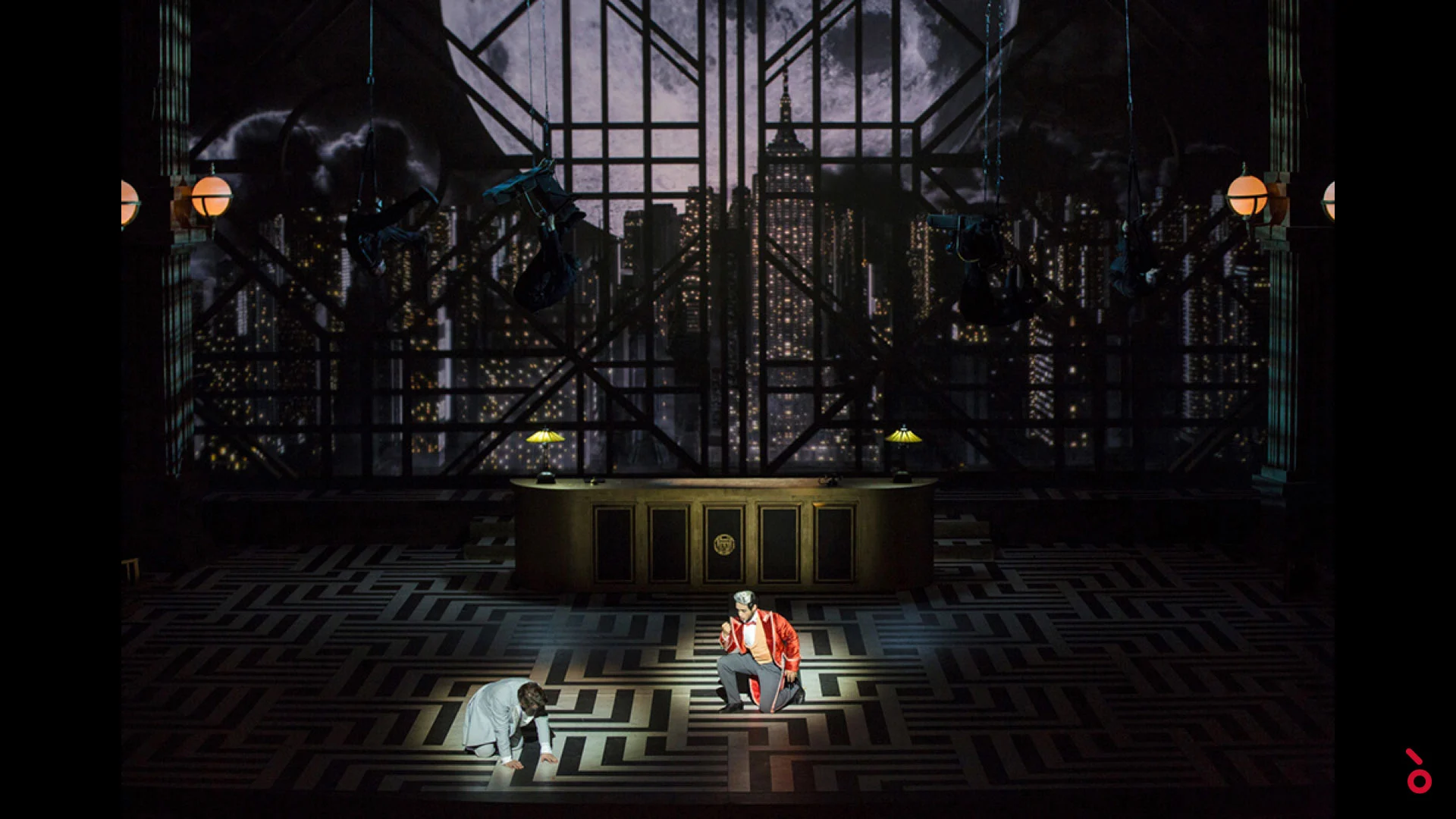 Due artisti su un pavimento a labirinto davanti a un bancone della reception e a un fondale di grattacieli notturni – The Opera! alla Royal Opera House Muscat, Oman, 2019 – scenografia