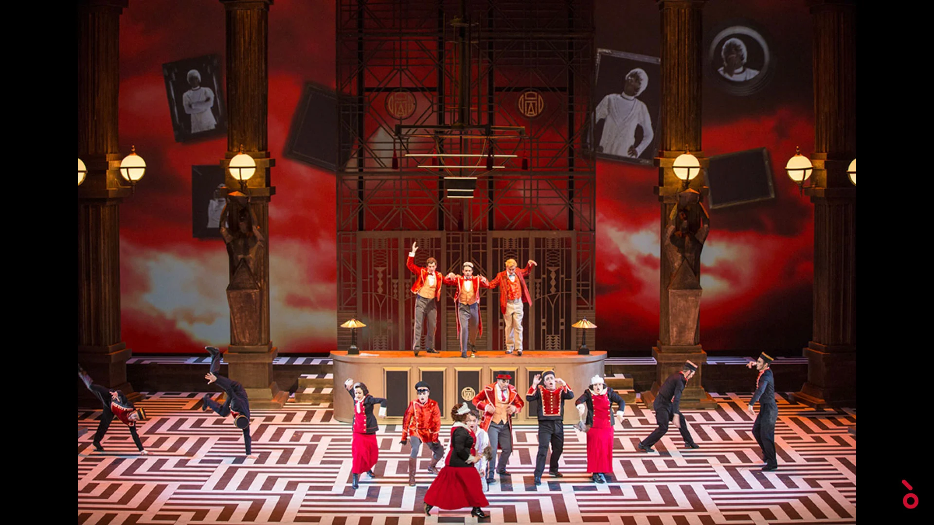 Fattorini che ballano su un pavimento a labirinto bianco e nero davanti a un fondale di cielo rosso con ritratti sospesi – The Opera! alla Royal Opera House Muscat, Oman, 2019 – scenografia