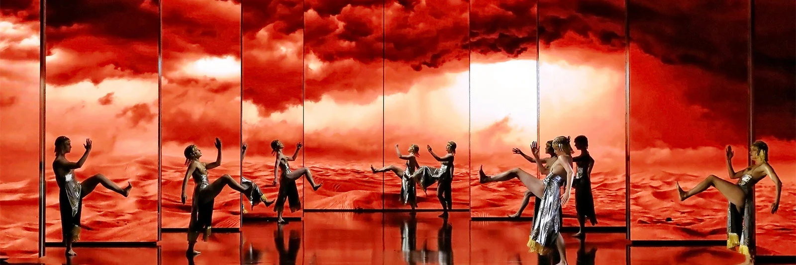 Danzatori in fila davanti a dieci schermi con dune rosse del deserto e nuvole infuocate – Aida alla Sydney Opera House, Australia, 2018 – scenografia d'opera