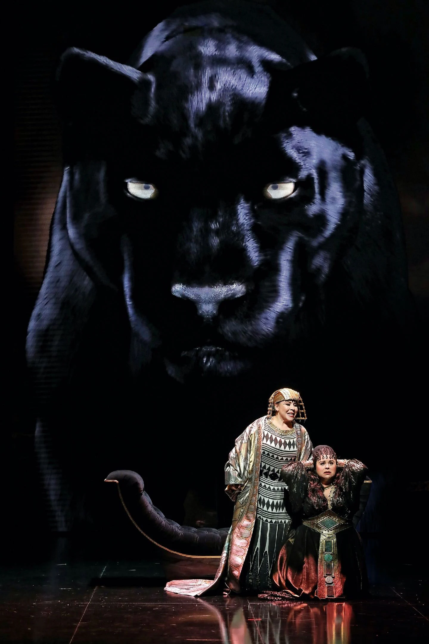 Due cantanti in costumi egizi inginocchiati sotto una gigantesca immagine video di una pantera nera – Aida alla Sydney Opera House, Australia, 2018 – scenografia d'opera