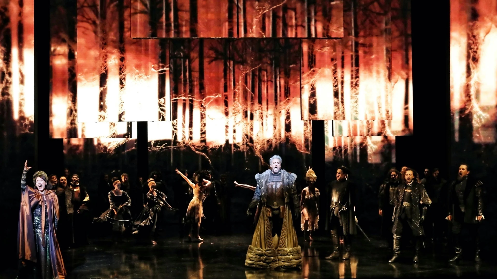 Anna Bolena in scena: la regina in abito dorato davanti al cast, sotto proiezioni di foreste in fiamme su pannelli sospesi – Anna Bolena alla Sydney Opera House, Australia, 2019 – scenografia d'opera