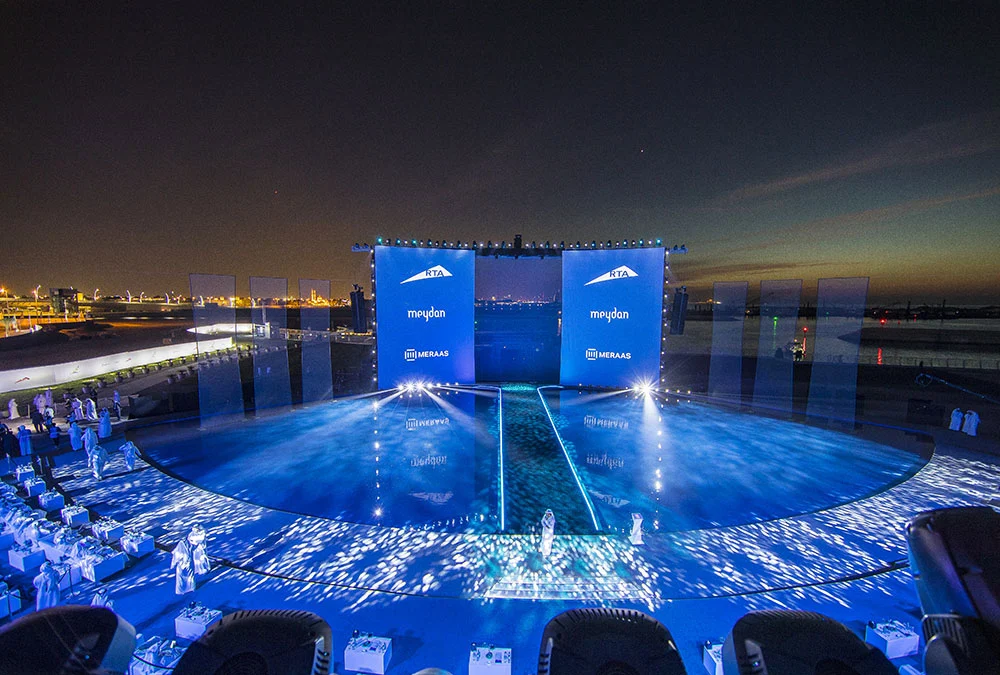 Ampia vista del palco galleggiante al crepuscolo: pavimento d'acqua blu, schermi degli sponsor e posti per gli ospiti lungo la riva – Cerimonia di apertura del Dubai Water Canal, Emirati Arabi Uniti, 2016 – progettazione di eventi