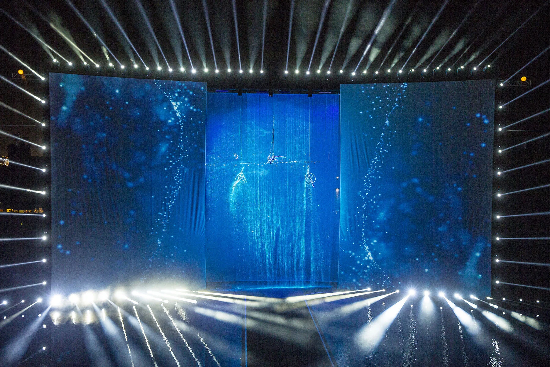 Palco della cerimonia di apertura sull'acqua: tre schermi illuminati di blu con artisti aerei sospesi sopra una cascata – Cerimonia di apertura del Dubai Water Canal, Emirati Arabi Uniti, 2016 – progettazione di eventi