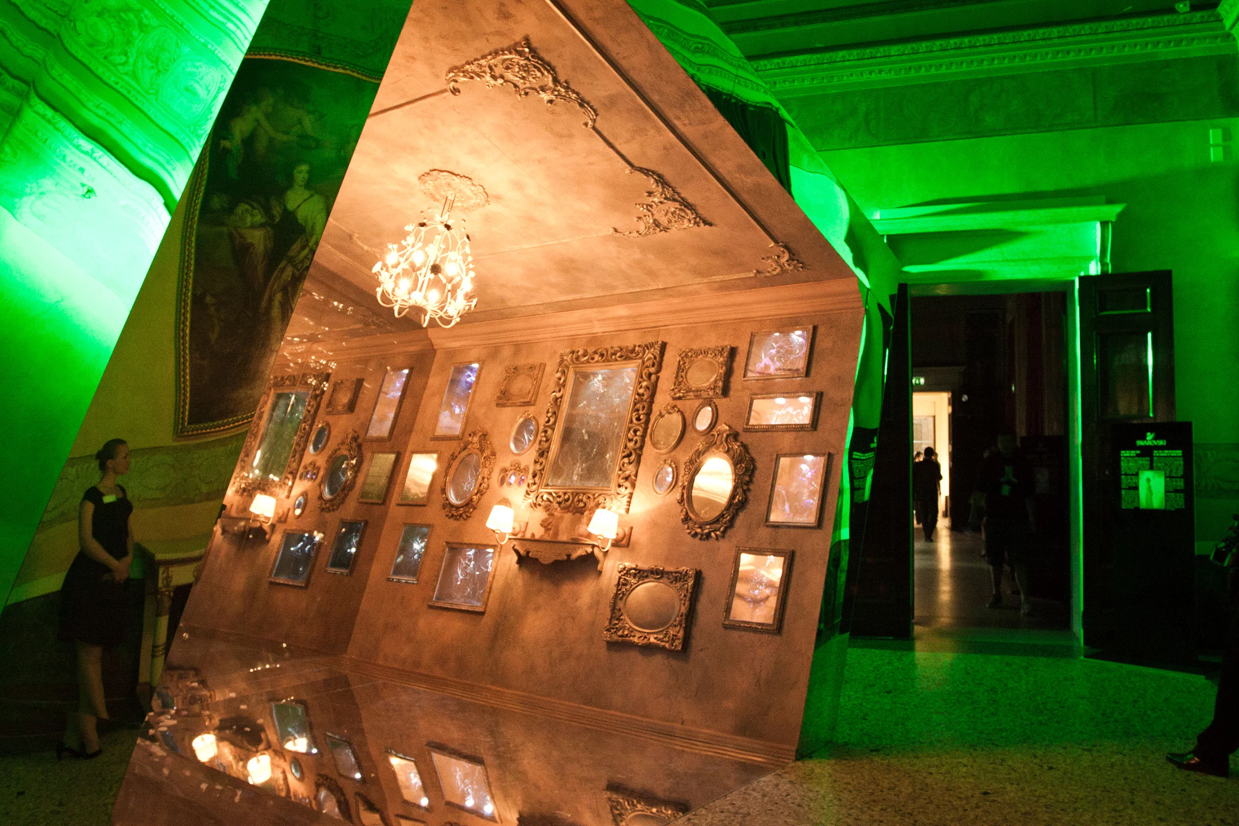 Pannello a specchio inclinato che riflette una sala di cornici dorate e un lampadario, in una sala in luce verde – Swarovski Fashionation Party a Palazzo Reale, Milano, Italia, 2011 – progettazione di eventi