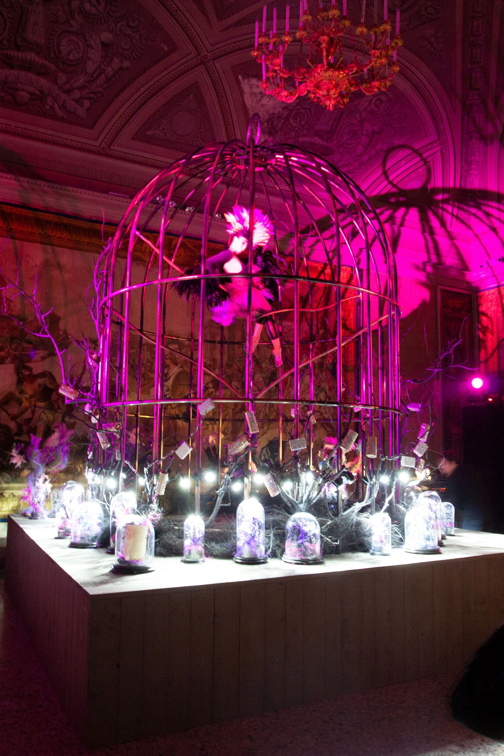 Gigantesca voliera su un basamento di legno in luce magenta, con una figura piumata all'interno e gioielli in campane di vetro – Swarovski Fashionation Party a Palazzo Reale, Milano, Italia, 2011 – progettazione di eventi
