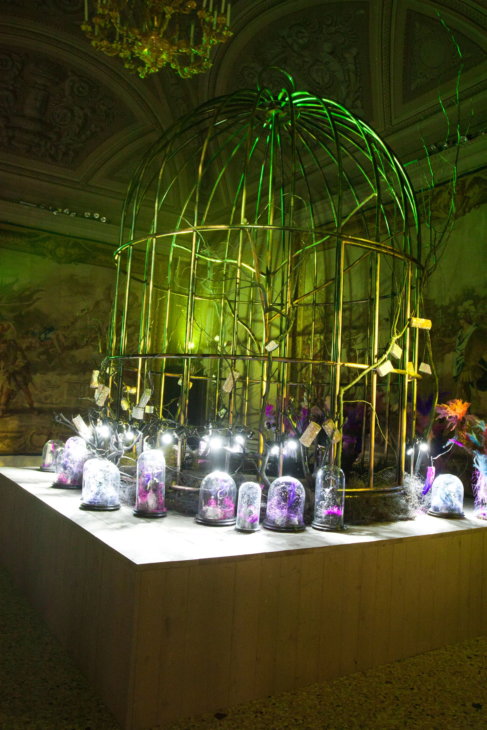 Voliera dorata in luce verde in una sala affrescata, circondata da campane di vetro con gioielli viola – Swarovski Fashionation Party a Palazzo Reale, Milano, Italia, 2011 – progettazione di eventi