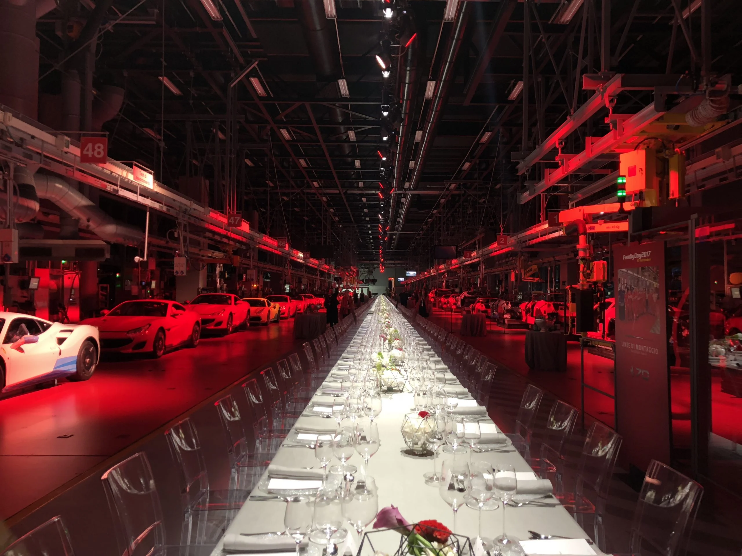 Lunga tavola imbandita in un capannone illuminato di rosso, auto Ferrari parcheggiate ai lati – Presentazione Ferrari Monza SP1, Maranello, Italia, 2018 – progettazione di eventi