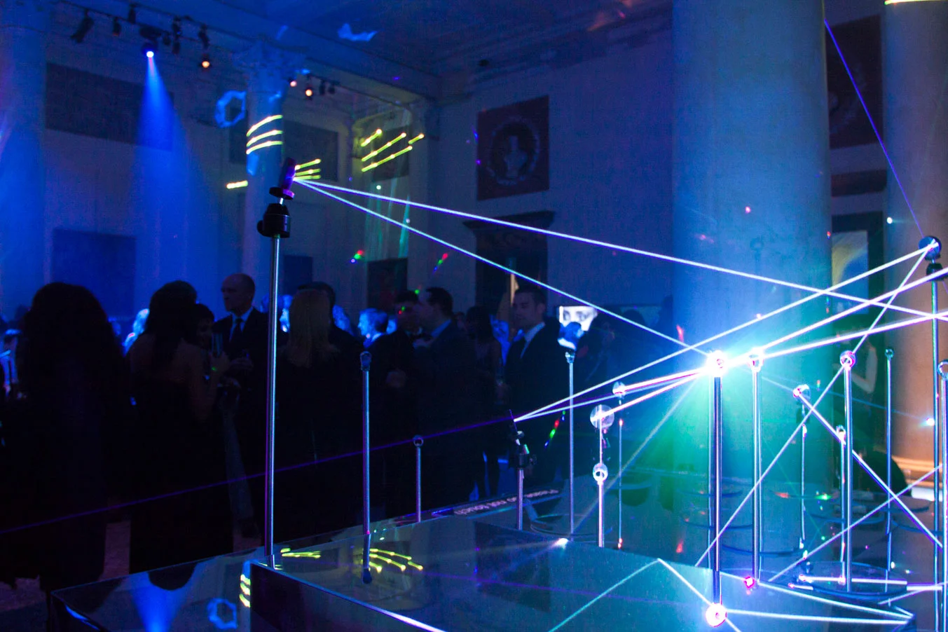 Ospiti in una sala illuminata di blu attraversata da linee laser tese tra sottili aste metalliche su una base a specchio – Swarovski Fashionation Party a Palazzo Reale, Milano, Italia, 2011 – progettazione di eventi