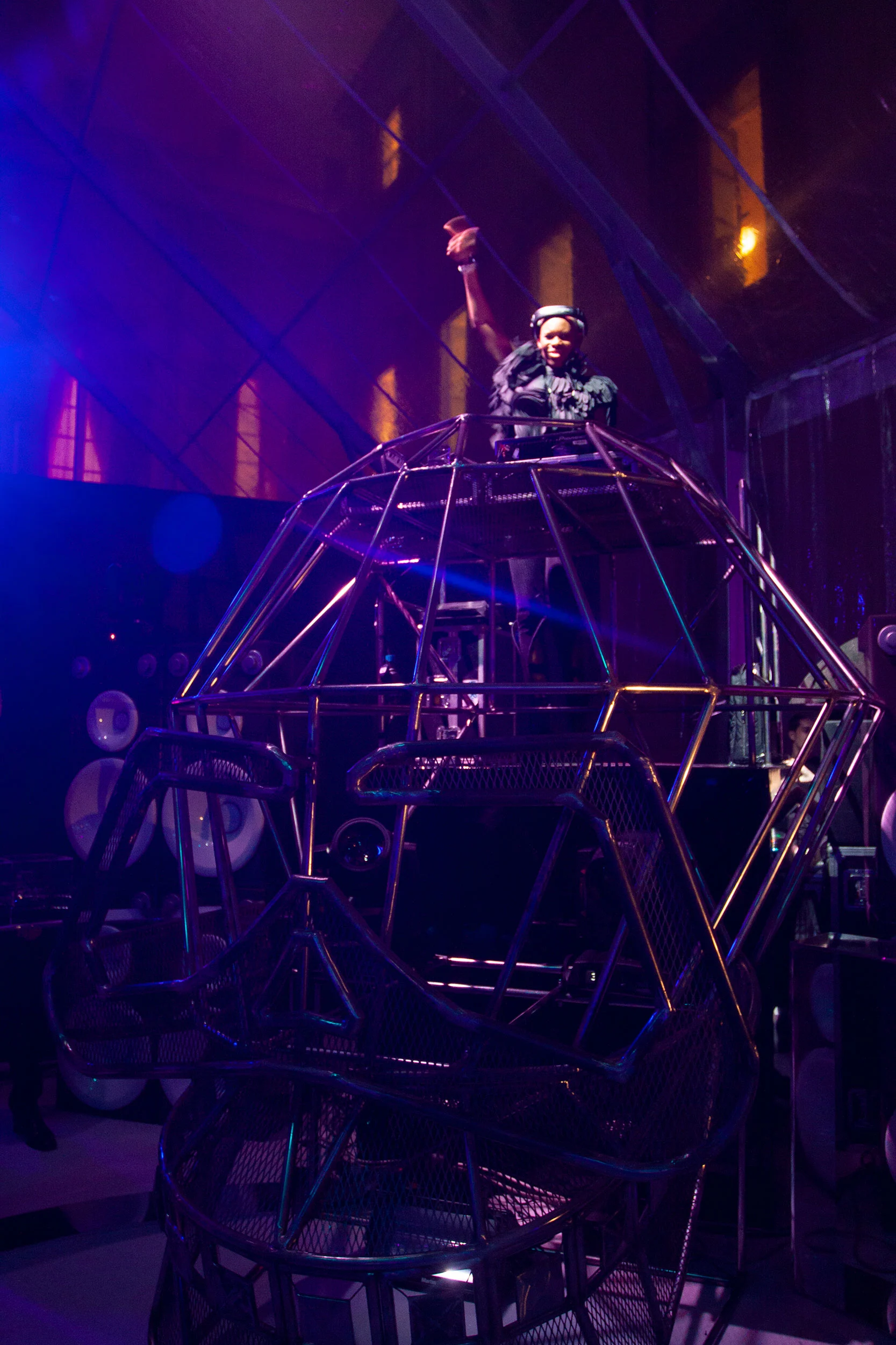 DJ con un braccio alzato in cima a un'alta consolle geometrica a telaio metallico a forma di testa, illuminata di viola – Swarovski Fashionation Party a Palazzo Reale, Milano, Italia, 2011 – progettazione di eventi