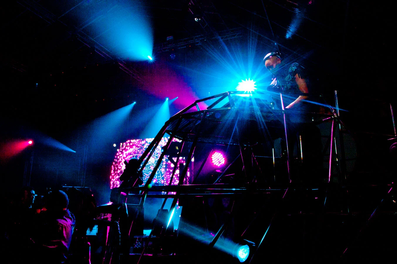 Consolle del DJ su una struttura a telaio metallico illuminata da fasci blu e rosa, con uno schermo LED sullo sfondo – Swarovski Fashionation Party a Palazzo Reale, Milano, Italia, 2011 – progettazione di eventi