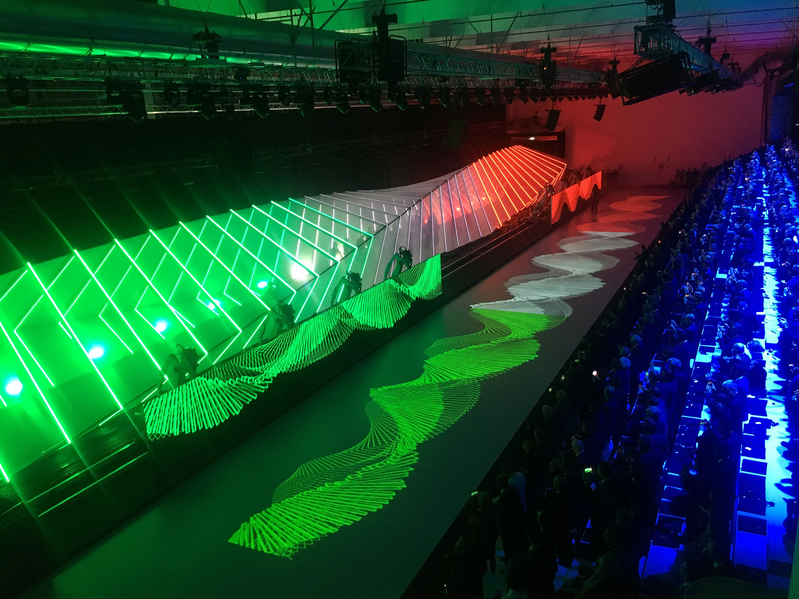 Struttura luminosa ondulata verde, bianca e rossa con un'onda proiettata a terra accanto al pubblico – Anteprima mondiale Lamborghini Urus, Sant'Agata Bolognese, Italia, 2017 – progettazione di eventi