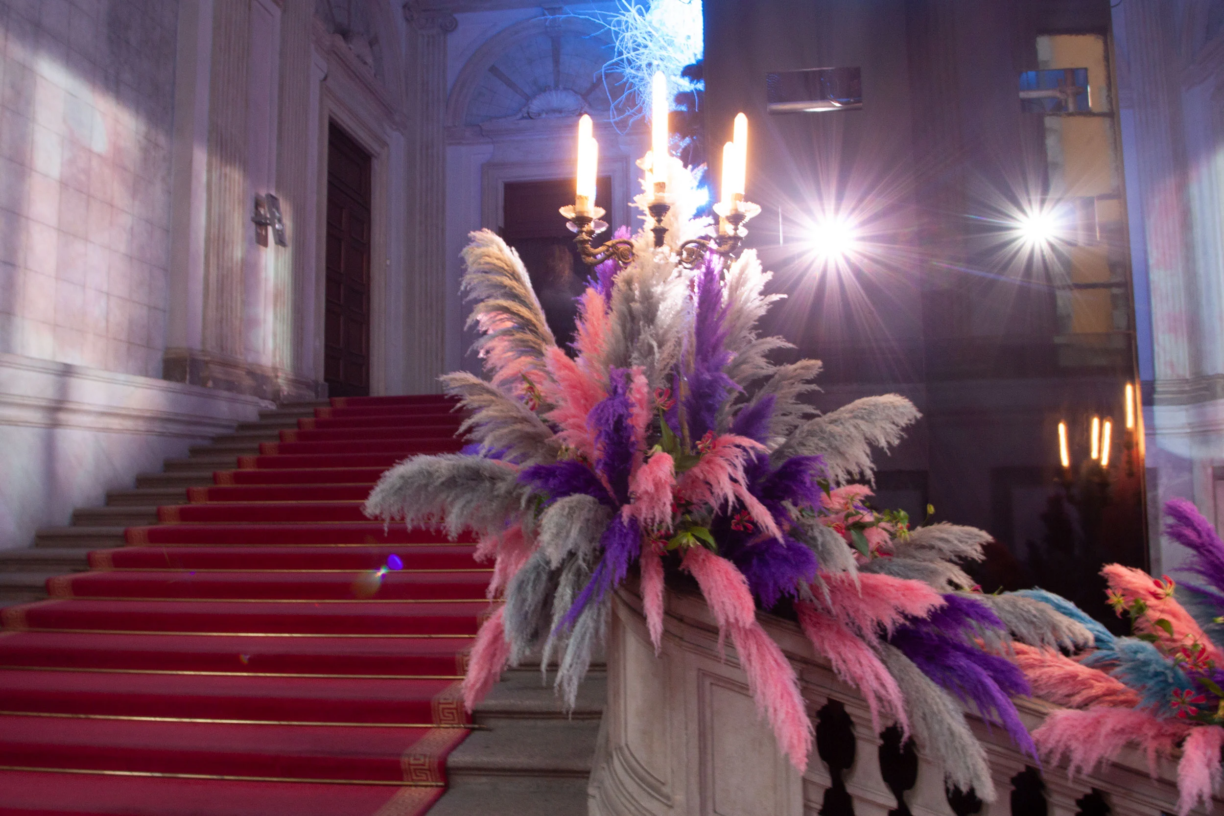 Scalone con tappeto rosso, candelabri e pennacchi di piume rosa, viola e grigie sulla balaustra – Swarovski Fashionation Party a Palazzo Reale, Milano, Italia, 2011 – progettazione di eventi
