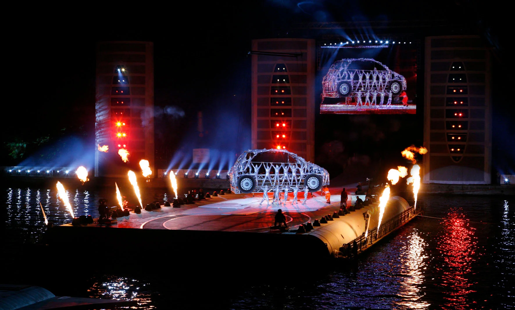 Palco galleggiante sul fiume Po con una Fiat 500 umana incorniciata dalle fiamme, una diretta sullo schermo sopra – Anteprima mondiale Fiat Welcome 500, Torino, Italia, 2007 – progettazione di eventi