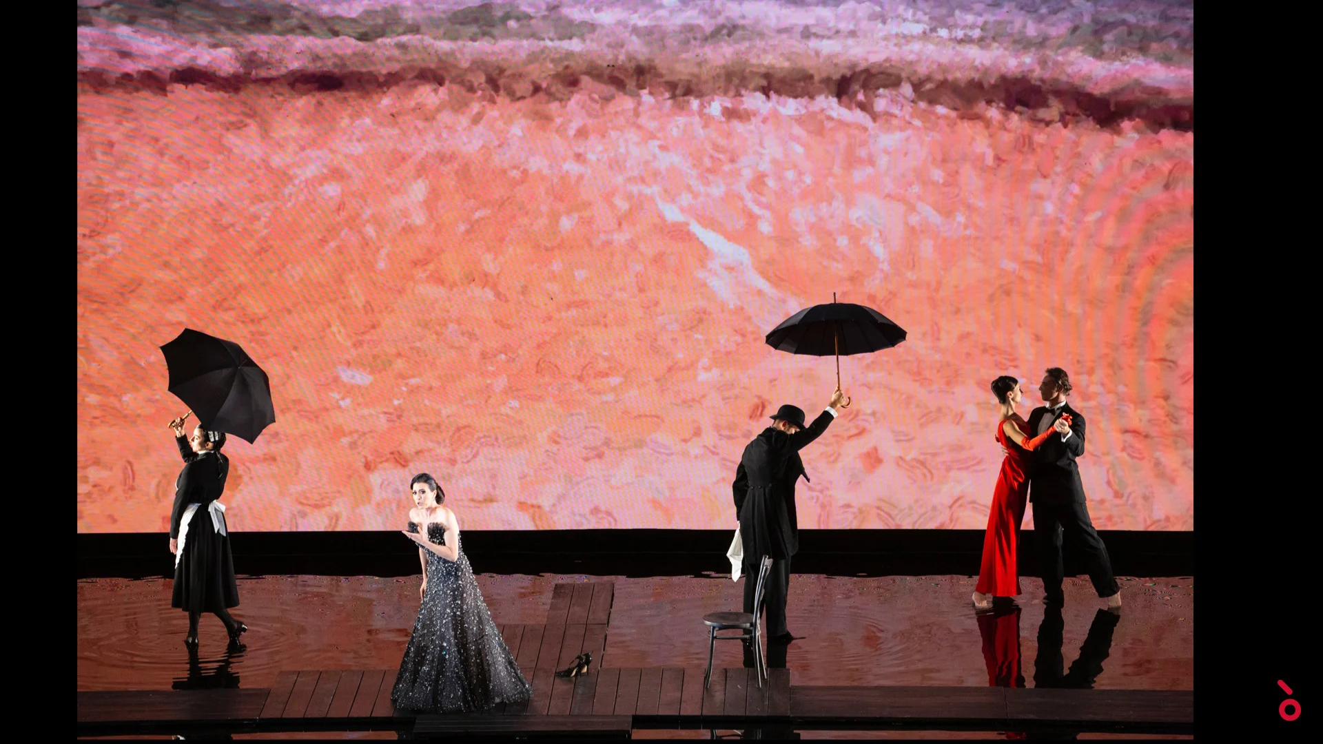 Artisti con ombrelli neri e una coppia che balla su una pedana in legno davanti a una proiezione rosso corallo – A Riveder le Stelle al Teatro alla Scala, Milano, Italia, 2020 – scenografia d'opera