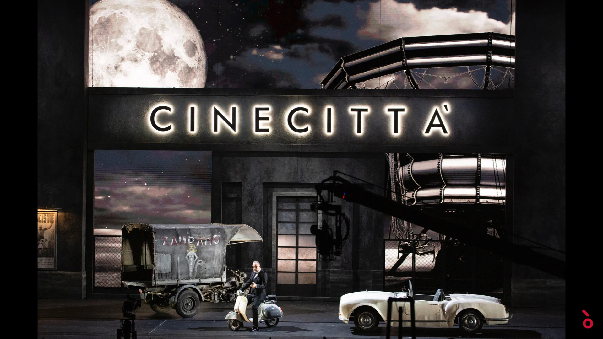 Scenografia con l'insegna illuminata di Cinecittà, una luna piena, uno scooter, un furgone d'epoca e una decappottabile bianca – A Riveder le Stelle al Teatro alla Scala, Milano, Italia, 2020 – scenografia d'opera