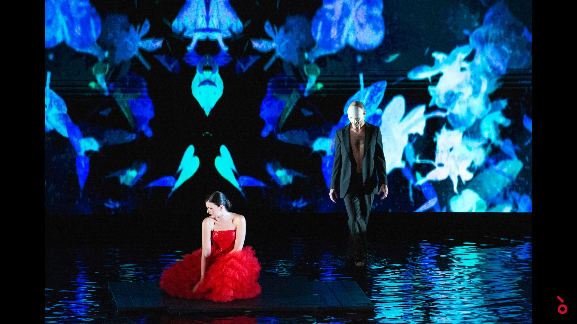 Ballerina in abito di tulle rosso su una pedana sopra un pavimento d'acqua, proiezione caleidoscopica blu alle spalle – A Riveder le Stelle al Teatro alla Scala, Milano, Italia, 2020 – scenografia d'opera