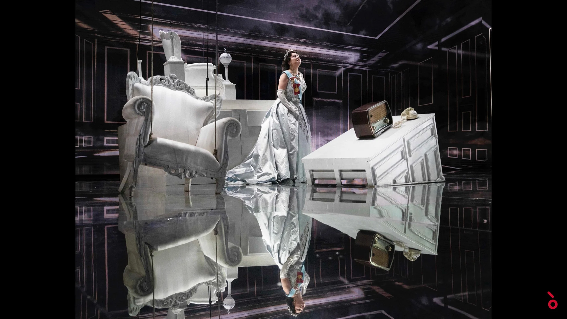 La regina in abito argento tra mobili barocchi bianchi, riflessa nel pavimento a specchio – Elisabetta, Regina d'Inghilterra al Rossini Opera Festival, Pesaro, Italia, 2021 – scenografia d'opera