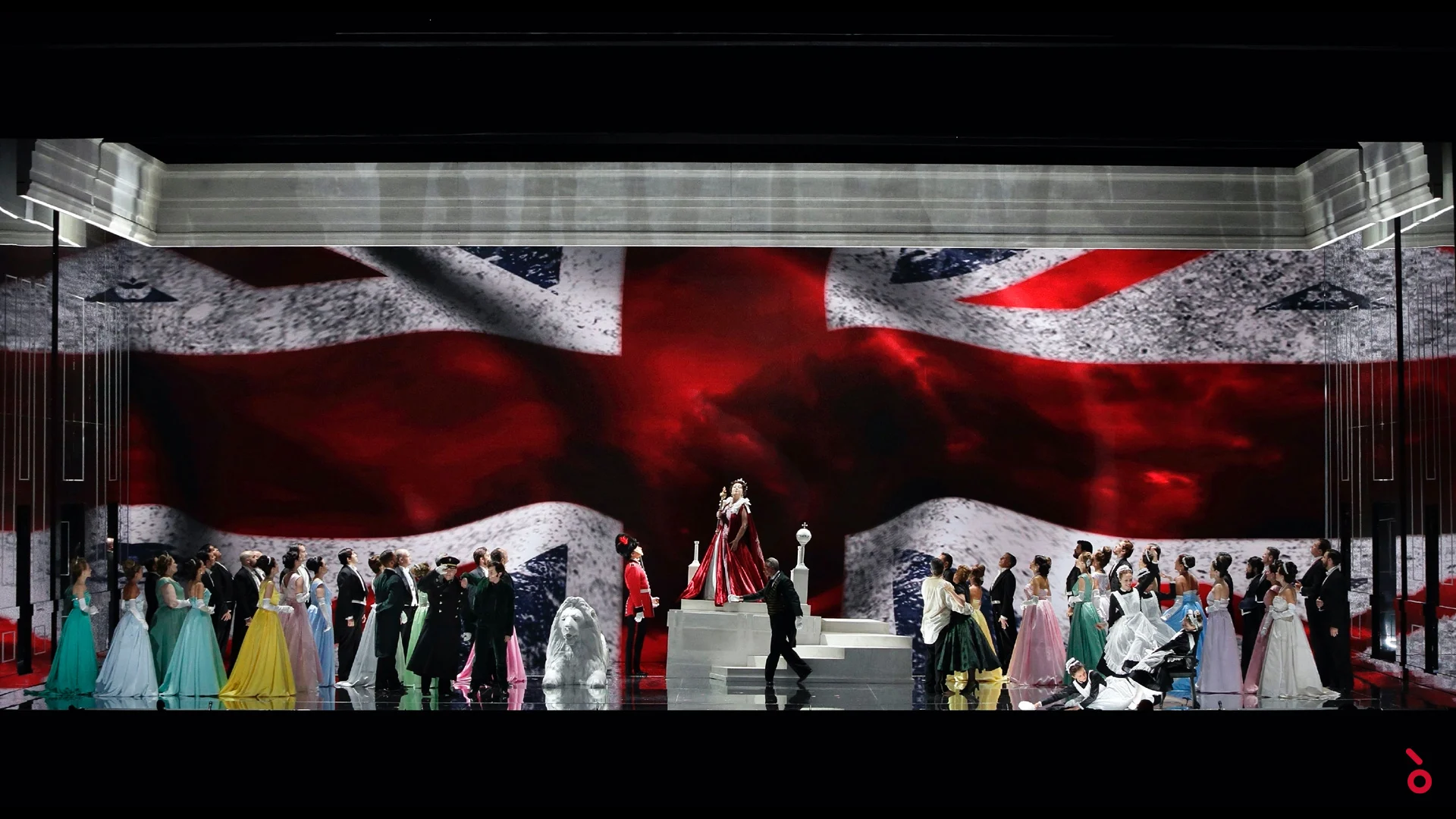 Tutto il cast in abiti colorati davanti a un'enorme proiezione della Union Jack, la regina su gradini bianchi – Elisabetta, Regina d'Inghilterra al Rossini Opera Festival, Pesaro, Italia, 2021 – scenografia d'opera