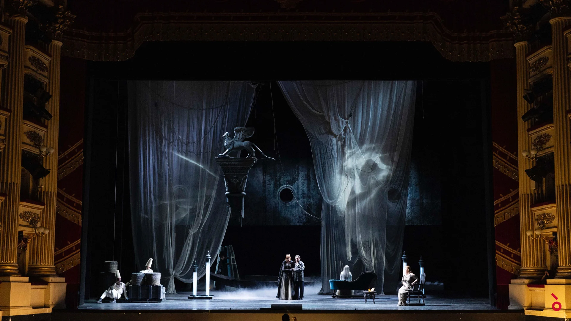 Scena intima tra tende grigie velate con proiezioni, la statua di un leone alato sospesa sopra il palco – La Gioconda al Teatro alla Scala, Milano, Italia, 2022 – scenografia d'opera