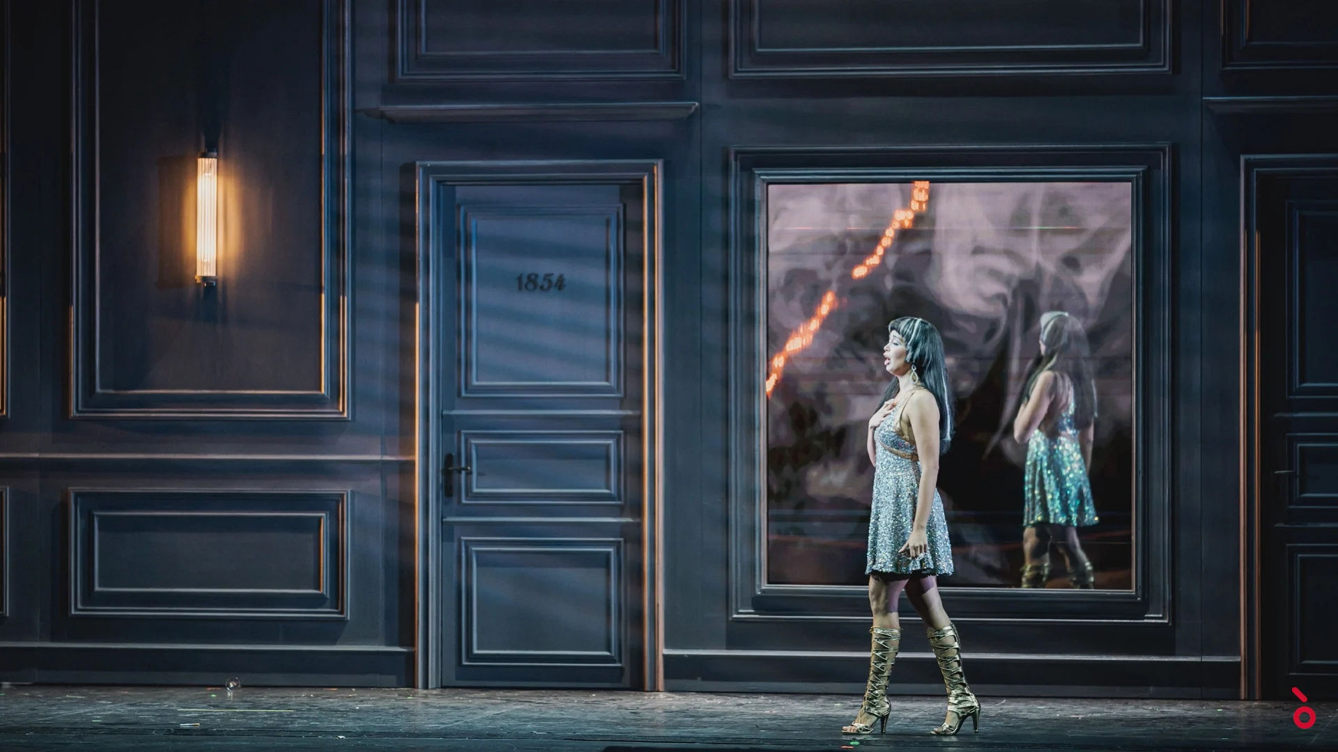 Cantante in abito di paillettes e stivali dorati che passa davanti a una porta numerata e a un pannello video a specchio – La Traviata al Maggio Musicale Fiorentino, Firenze, Italia, 2022 – scenografia d'opera