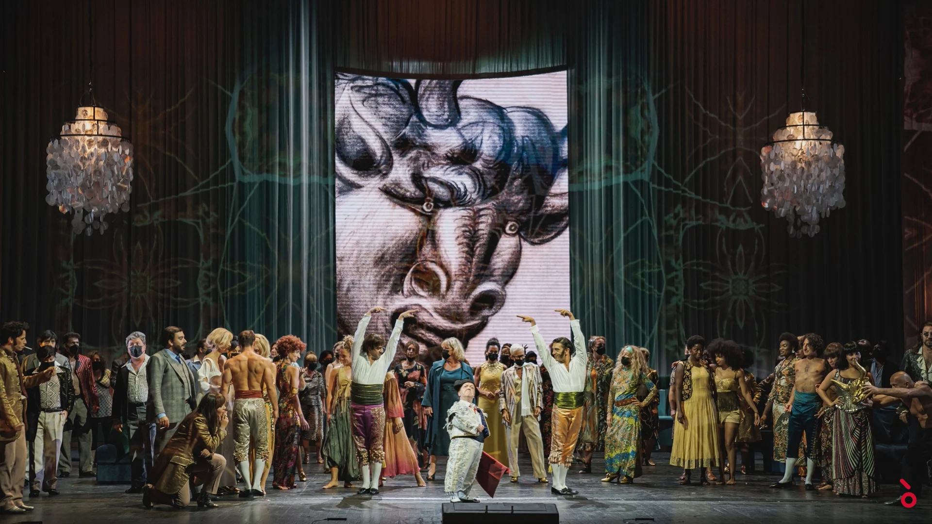 Coro in abiti colorati anni Sessanta davanti all'enorme disegno proiettato di un toro, lampadari di cristallo ai lati – La Traviata al Maggio Musicale Fiorentino, Firenze, Italia, 2022 – scenografia d'opera