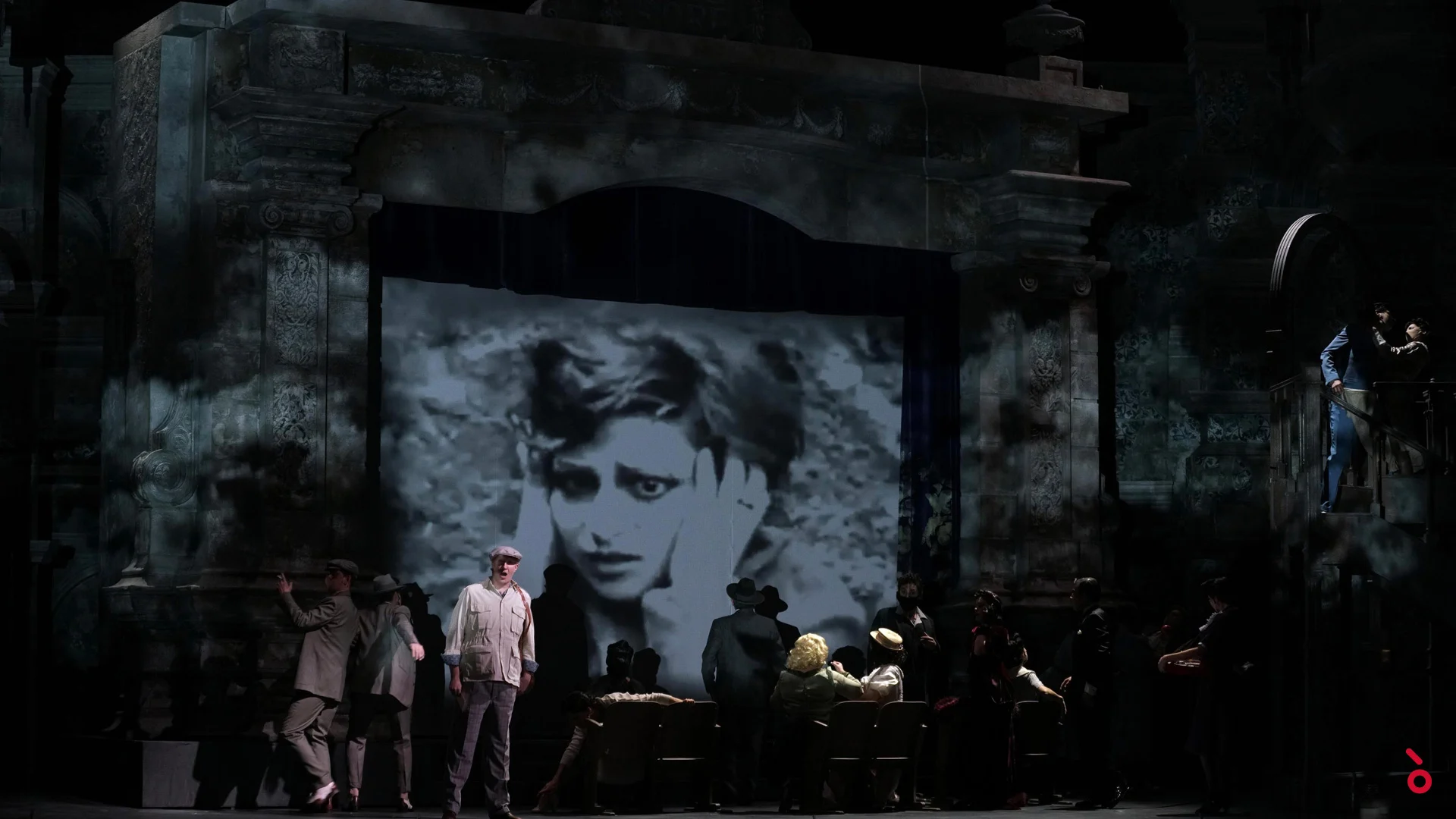 Primo piano cinematografico in bianco e nero di una donna proiettato nell'arco del cinema sopra artisti in abiti d'epoca – Luisa Fernanda al Teatro de la Zarzuela, Madrid, Spagna, 2021 – scenografia d'opera