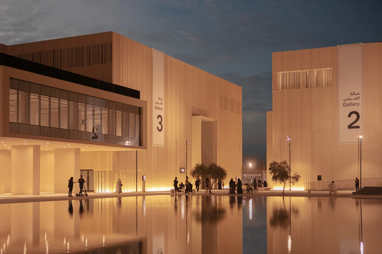 Gallery 2 e 3 illuminate di notte, visitatori che camminano lungo la vasca a specchio tra i padiglioni – Biennale delle Arti Islamiche, Jeddah, Arabia Saudita, 2023 – architettura