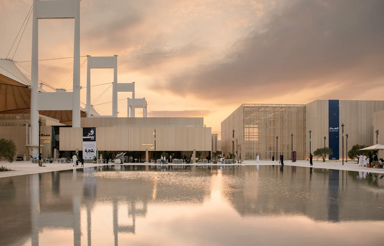 Padiglioni della Biennale al tramonto accanto ai piloni bianchi delle tende dell'Hajj Terminal, riflessi in una vasca a specchio – Biennale delle Arti Islamiche, Jeddah, Arabia Saudita, 2023 – architettura