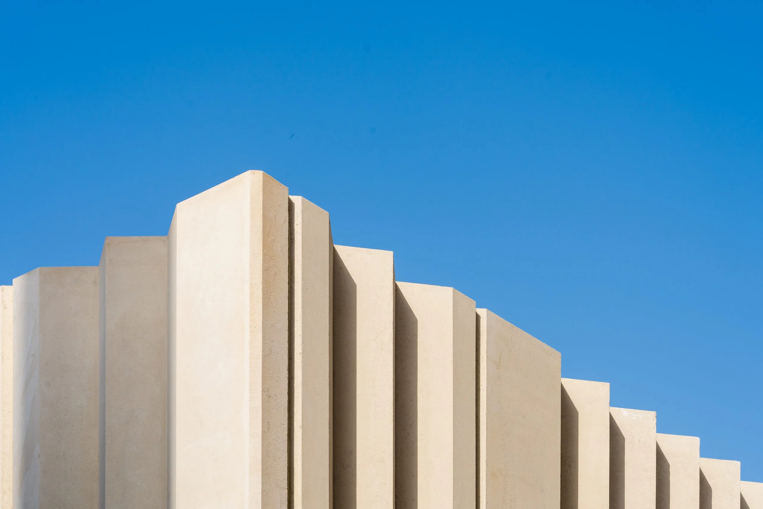 Lamelle beige a gradoni della parete di un padiglione che si stagliano contro un cielo blu intenso – Biennale delle Arti Islamiche, Jeddah, Arabia Saudita, 2023 – architettura