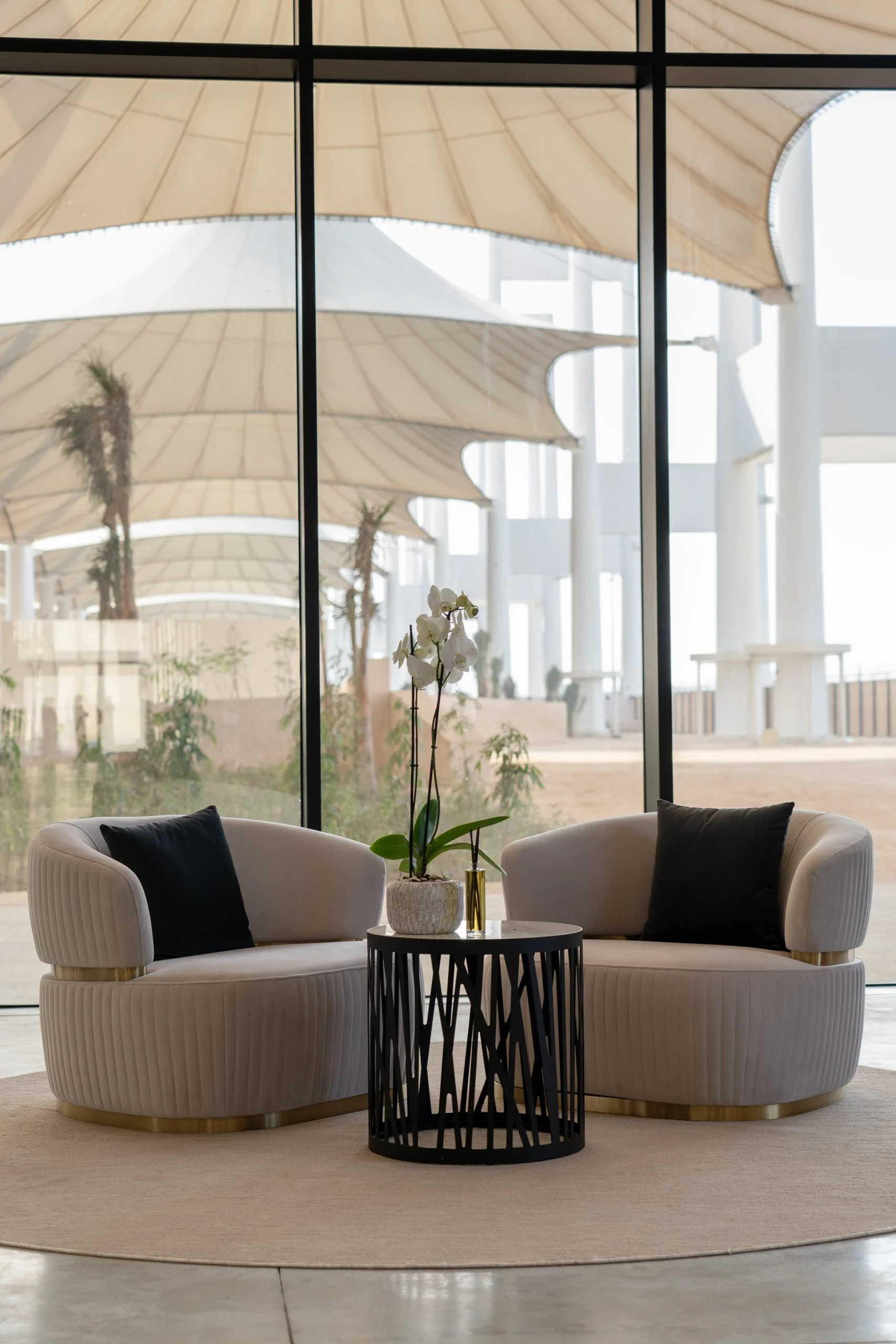Lounge con due poltrone curve e un'orchidea davanti a una vetrata affacciata sulle coperture bianche a tenda – Biennale delle Arti Islamiche, Jeddah, Arabia Saudita, 2023 – architettura