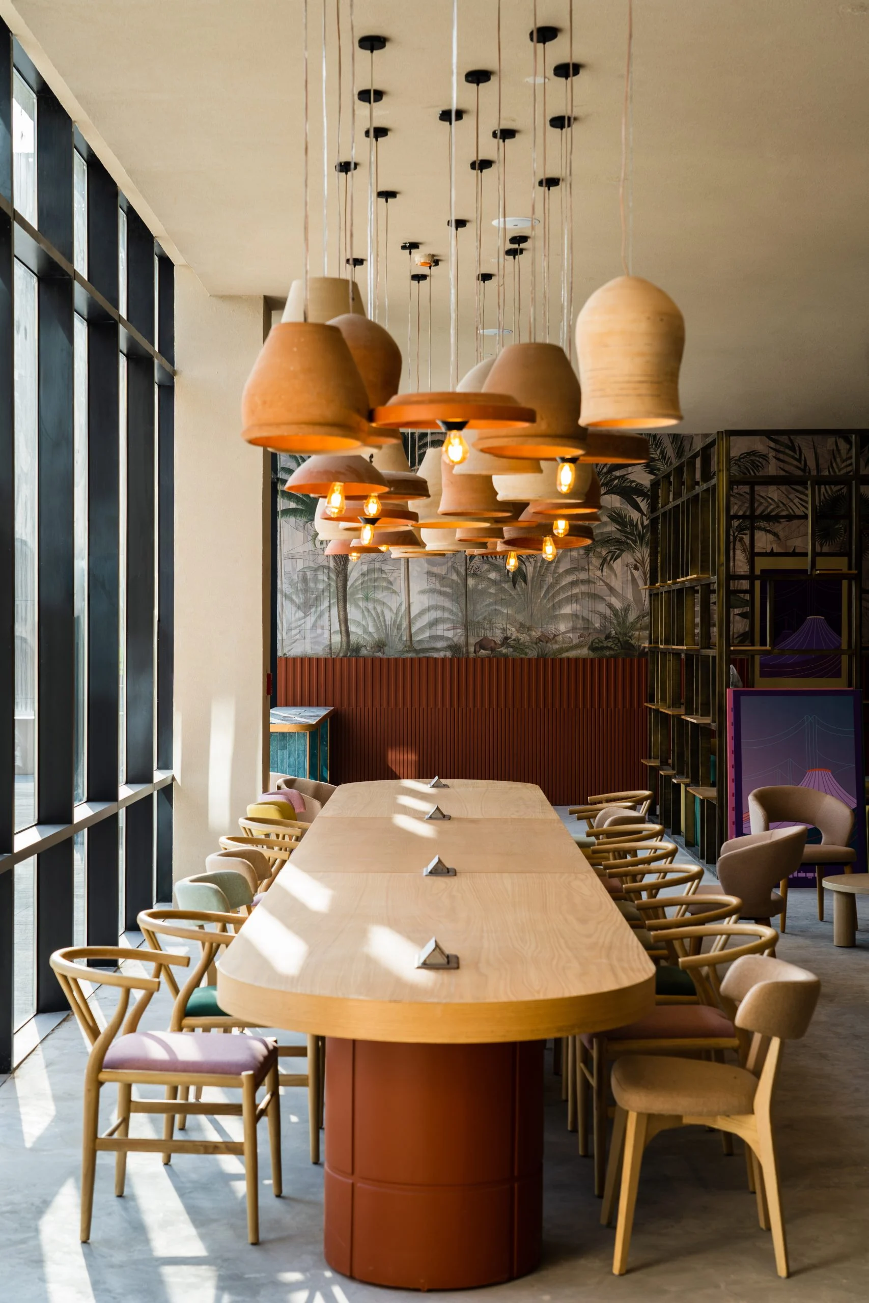 Lungo tavolo comune in legno sotto gruppi di lampade a sospensione in terracotta, accanto a vetrate a tutta altezza – Biennale delle Arti Islamiche, Jeddah, Arabia Saudita, 2023 – architettura