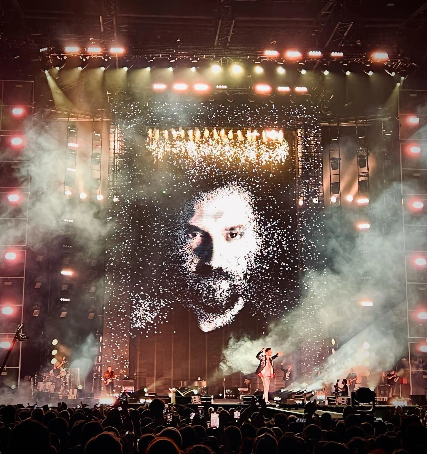 Enorme parete LED con il volto del cantante in particelle scintillanti, fumo e la band sul palco sotto – Cesare Cremonini Stadi 2022, Italia – scenografia per concerti