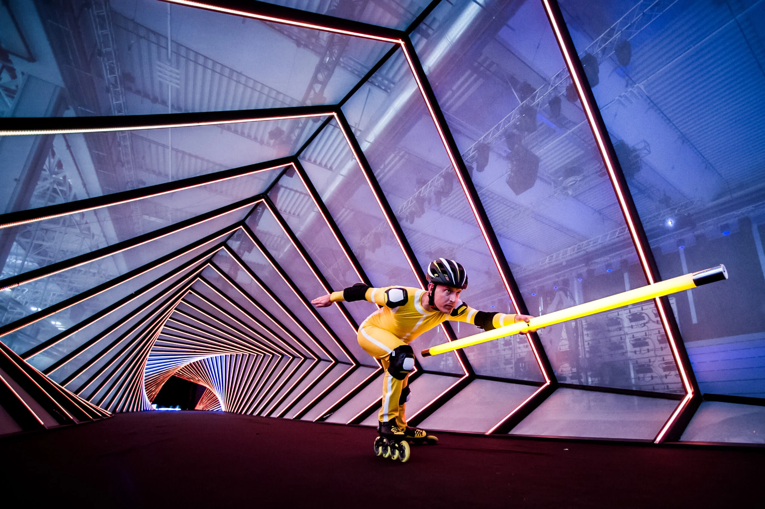 Pattinatore in linea in tuta gialla che porta un tubo luminoso in un tunnel di cornici di luce inclinate – Anteprima mondiale Lamborghini Urus, Sant'Agata Bolognese, Italia, 2017 – progettazione di eventi