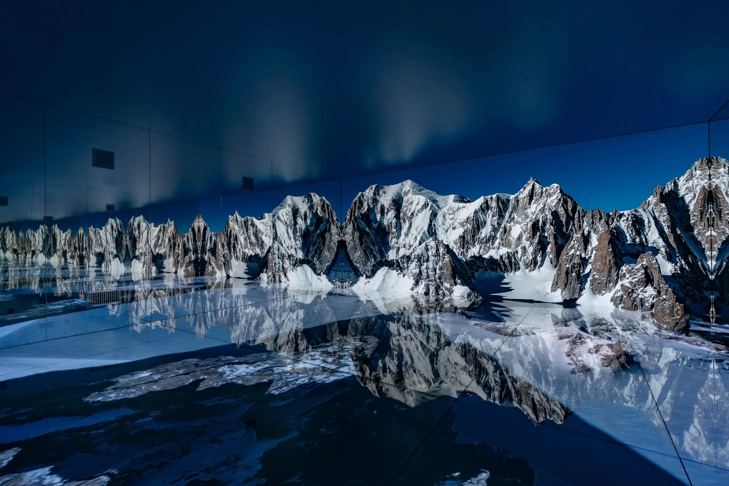 Panorama del massiccio del Monte Bianco sulla parete LED, con le vette riflesse sul pavimento a specchio scuro – Mont Blanc Infinity Room allo Skyway, Courmayeur, Italia, 2023 – progettazione di installazioni