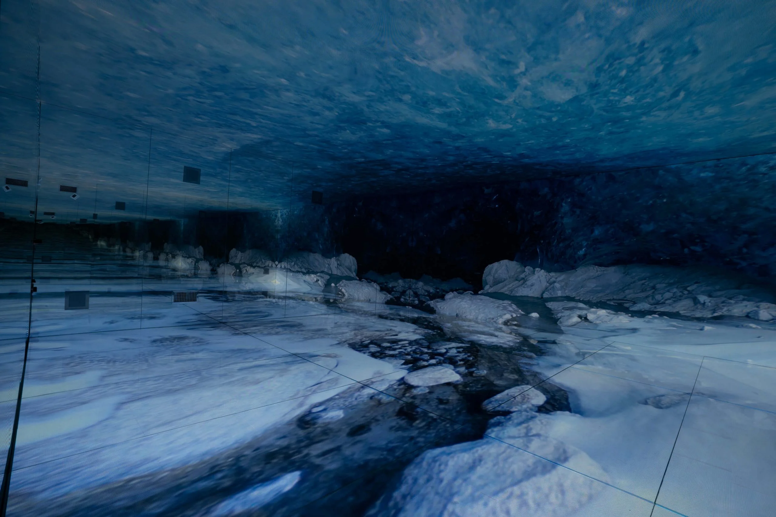 Stanza immersiva che ricrea una grotta glaciale blu, con blocchi di ghiaccio sul pavimento e sul soffitto LED – Mont Blanc Infinity Room allo Skyway, Courmayeur, Italia, 2023 – progettazione di installazioni