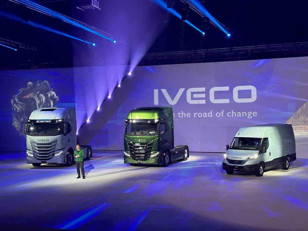 Presentatore sul palco accanto a due camion e un furgone, il logo Iveco sul fondale LED – Lancio IVECO Be The Change, Barcellona, Spagna, 2023 – progettazione di eventi