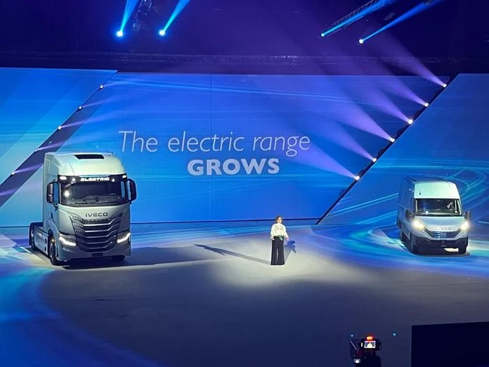 Presentatore tra un camion elettrico e un furgone, sullo schermo la scritta The electric range grows – Lancio IVECO Be The Change, Barcellona, Spagna, 2023 – progettazione di eventi