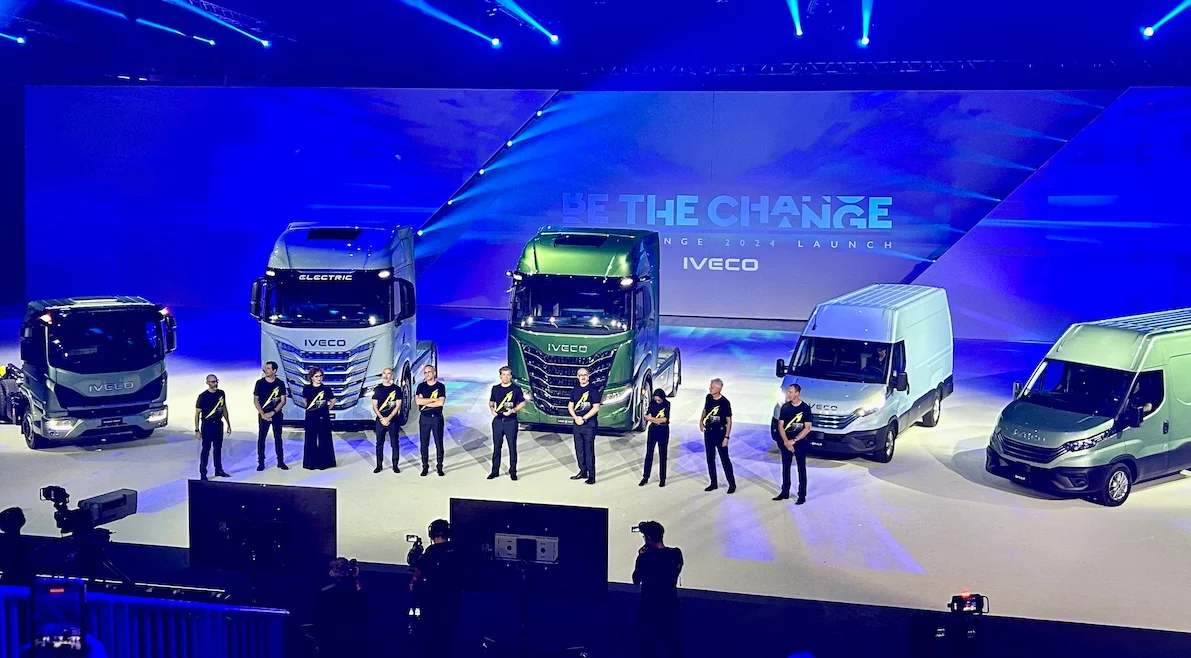 Camion e furgoni Iveco allineati sul palco di Be The Change, presentatori in piedi davanti – Lancio IVECO Be The Change, Barcellona, Spagna, 2023 – progettazione di eventi