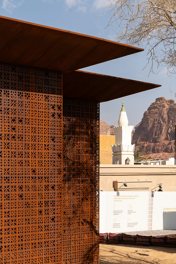 Angolo dello schermo in metallo forato e dello sbalzo del tetto, un minareto bianco e speroni di roccia rossa dietro – Design Space AlUla, Arabia Saudita, 2024 – architettura